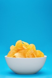 Potato chips or crisps in white bowl on blue background