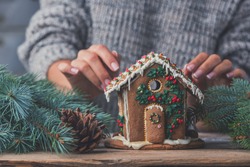 Gingerbread house and women's hands in sweater, the concept of preparation for the Christmas holidays

