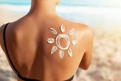 Sun Protection.Sun Cream. Woman Applying Sun Cream on Tanned  Shoulder In Form Of The Sun. Skin and Body Care. Girl Using Sunscreen to Skin. 