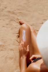 Closeup on female Hand applying solar  sun cream  on Leg. Skincare. Sun protection. Woman smear sunscreen moisturizing lotion on her smooth tanned legs. Girl Holding Sunblock. 