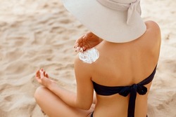 Woman applying sunscreen creme on  tanned  shoulder. Skin care. Body Sun protection sun cream. Bikini hat woman applying moisturizing sunscreen lotion on back.