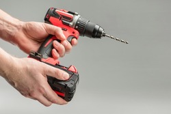 a man's hand removes the battery from a cordless tool. A man inserts a battery into a screwdriver. Repair and construction concept on gray background