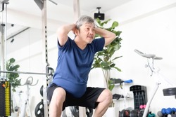 Gray-haired senior man doing squats at the gym

