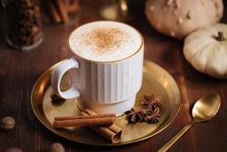 Cup of pumpkin spice late with cinnamon sticks, pumpkins star anise and nutmeg in a rustic moody and vintage atmosphere