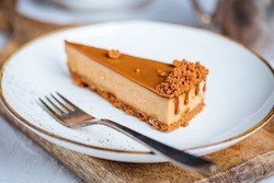 A piece of caramel cheesecake with cookie crumbs on top. Creamy three layer cake on bright plate. Popular American dessert.