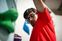 Man stretching his arm to reach a climbing hold on a climbing wall