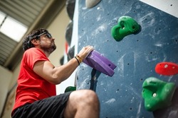 Man looking up holding a climbing hold on a climbing wall