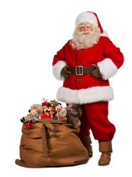 Full length portrait of a Santa Claus posing near a bag full of gifts isolated on white background