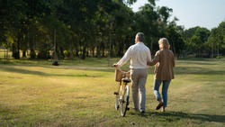 Caucasian elderly couples walking with a bicycle in the natural autumn sunlight garden feel cherish and love, concept elderly love, warm family, Happier Old-Age, retirement lifestyle.