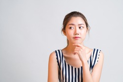 Portrait of young charming Asian woman looks pensive and curious thinking up and look sideways at grey background with copy space to the left, concept pensive thought woman, curious thinking woman.