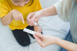 Adorable Asian girl kid pay attention with swab test process by her parent. Rapid self test for covid-19, Antigen test kit, quick check before school. new normal routine for kid. Selective focused.