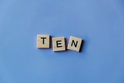 Number ten laid out from tiles in words. Wooden tiles on a blue background with letters. View from above. Copy space.