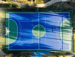 Aerial view of blue multi-sport court in the park. Used to practice football, basketball or volleyball. Top view. Sunny day. Sunset. Drone photo.