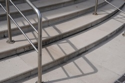 Concrete steps with deep contrasting shadow lines. Urban architectural modern chrome steel hand rail.
