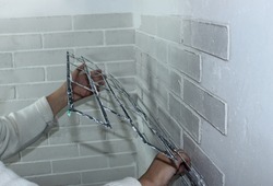 Close-up - a woman's hand removes the stencil from the decorative plaster on the wall. House renovation, decorative brick-like plaster on the wall. Make a brick wall at home with your own hands