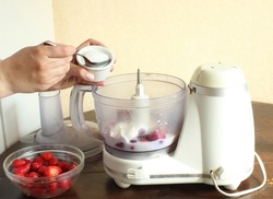 Close-up of a woman preparing a strawberry milkshake, spooning sugar into a food processor with a tablespoon. Strawberry milkshake recipe step by step