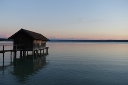 sunset and wooden footbridge and wooden House in the Lake in germany, Ammersee with beautiful sunset lights and the alps in the background 