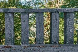 Old gray concrete fence with columns and railings in the park against the background of trees.