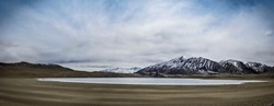 Panorama view of semi-frozen Kyagar Tso Lake, surrounded by snow-capped mountains