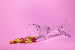 Colorful pills and elegant glass on pastel pink background. Taking too much pills as a part of modern lifestyle. Vitamins concept.