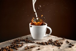 Splash studio shot of coffee beans and milk falling in to the white cup full of coffee.