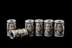 Several rolled-up bundles of 100 American dollars bills on a black background