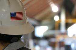 Rear portrait photo behind a female construction worker on a building job site. American flag on back of her white hard hat. Woman foreman in charge of successful development team.