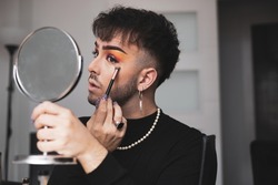 a young gay man puts on makeup by looking in the mirror at home to go out on the street.