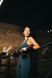 An Asian girl resting on the ropes of a boxing ring after a training, the girl looks to the side, Asian youth boxing.