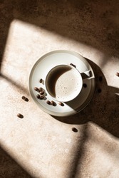 A cup of cappuccino or latte with coffee beans top view with shadows on beige background. Top view, copy space. Vertical orientation