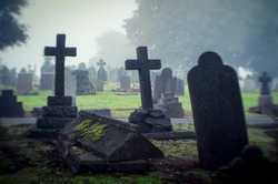 Misty view of dark stone crosses and tombstones in a deserted graveyard