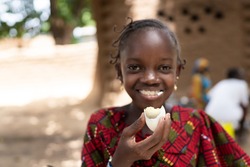 In this image, a smart black African girl is eating a boiled egg with great delight