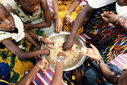 Group of African girls sitting on a mat, dividing their frugal meal, eating with their hands from a large metal plate