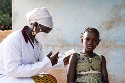 Tense little African schoolgirl is waiting for her pediatrician to inject a dose of vaccine into her arm