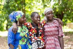 Three beautiful black African adolescent girls in colourful traditional outfit embracing each other; friendship concept