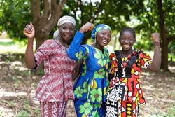 Group of young black African villagers in colourful traditional dresses smiling at the camera with their clenched fists as a symbol for women's strength and gender equality