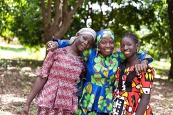 Three radiant young African women in beautiful traditional dresses looking at the camera; human relationship concept