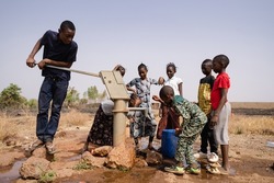 Group of African school age children gathering around a sub saharian village faucet collecting water for their families: Recurrence of World Water Day