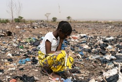Exhausted little African girl kneeling in a garbage dump where she is forced to search for reusable material; child labor and exploitation