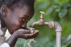 Beautiful African Child Drinking from a Tap (Water Scarcity Symbol).

Young African girl drinking clean water from a tap. Water pouring from a tap in the streets of the African city Bamako, Mali.