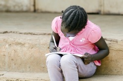 Close-Up of African Little Black Girl Writing notes sitting outside of her school building (classroom). Education schooling symbol.