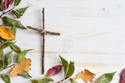 Wood cross with autumn leaf border on white wood background 