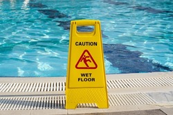 caution wet floor warning sign near swimming pool in hotel.