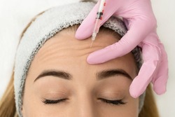 Close-up of the hands of an expert cosmetologist injecting botox into a woman's forehead. Correction of forehead and eye wrinkles with botulinum toxin.