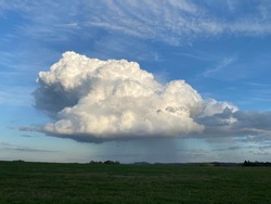 Ennepetal, Germany - October 22, 2020 - A white blue cumulus cloud in the blue sky from which you can see the rain falling.
