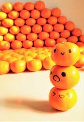 Tangerine with a face drawn with three oil-based pens piled up against the background of a large amount of oranges