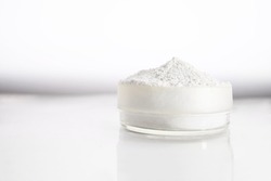 A container with zinc oxide on a white blurred background with reflection. Chemistry, health care, cosmetics production.