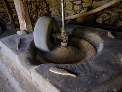A stone water mill grinding rice seeds, the rock of the mill is spinning, motion seems blurry and there are three wood spoons on the mill, rice seeds are being pressed.