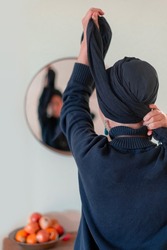 Religious Jewish woman puts a shawl on her head in front of a mirror. Back view