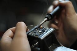 A female electronics technician is shown in close-up in a professional workshop while working with tin soldering parts. She repairs electronic devices and handles electrical equipment. She is solderin